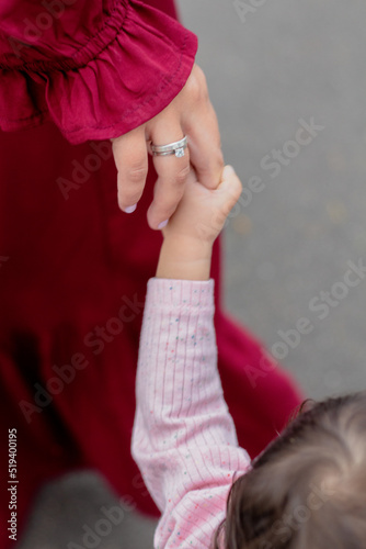 Cute baby girl holding hand with her mother. Aesthetic baby fashion.