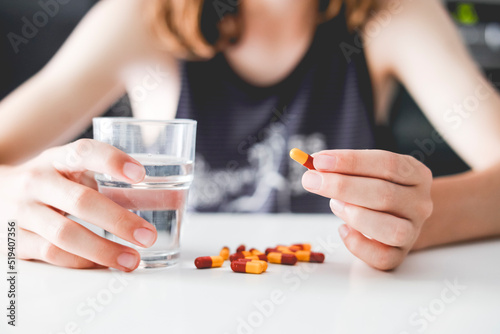 Close-up of a person sitting at a table with a glass of water and a stack of pills photo