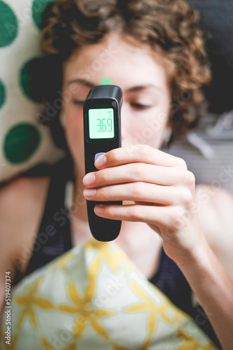 Teenager lying in bed taking his temperature with a digital thermometer photo
