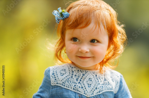 Bild auf Leinwand Cute portrait of baby red hair girl in blue dress sitting on a big tree stump in the park, looking at something invisible during sunset