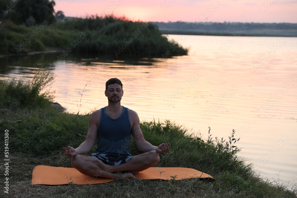 Man meditating near river in twilight. Space for text