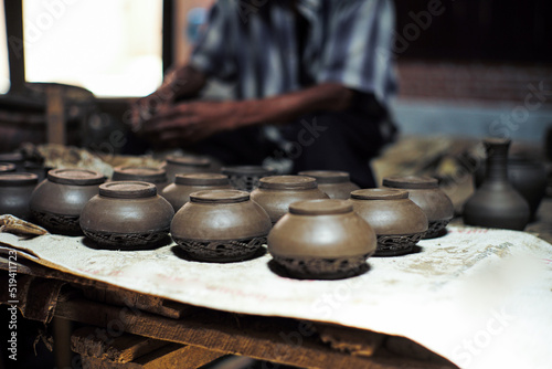 Group of clay jars in the production process with defocused old worker molding the clay work in background