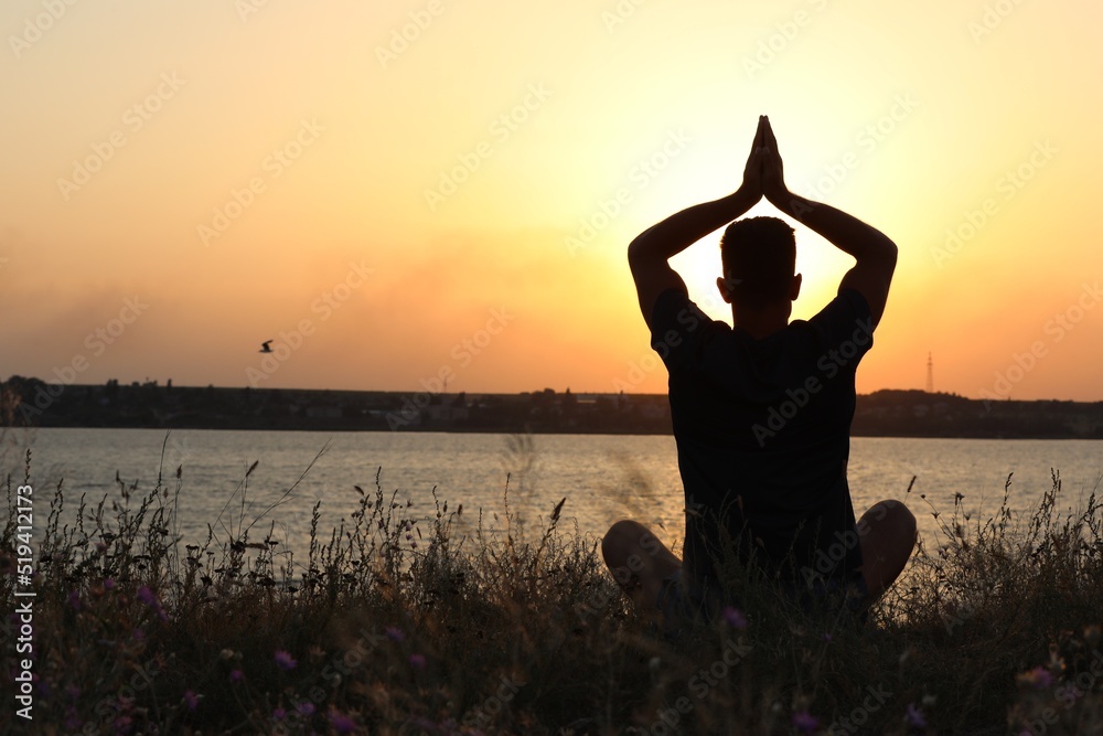 Man meditating near river at sunset, back view. Space for text