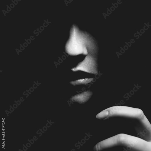 Black and white part of woman face with reaching hand with nails in black shadow background with copy space. Nose is in camera focus. Selective focus and image with shallow depth of field