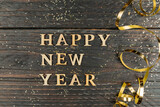 Happy new year inscription made with wooden letters decorated festive golden serpentine on wooden background wih copy space. Greeting card for new year celebration
