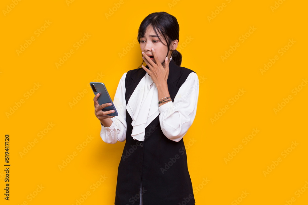 mad and shock young asian beautiful woman using mobile phone isolated on yellow background