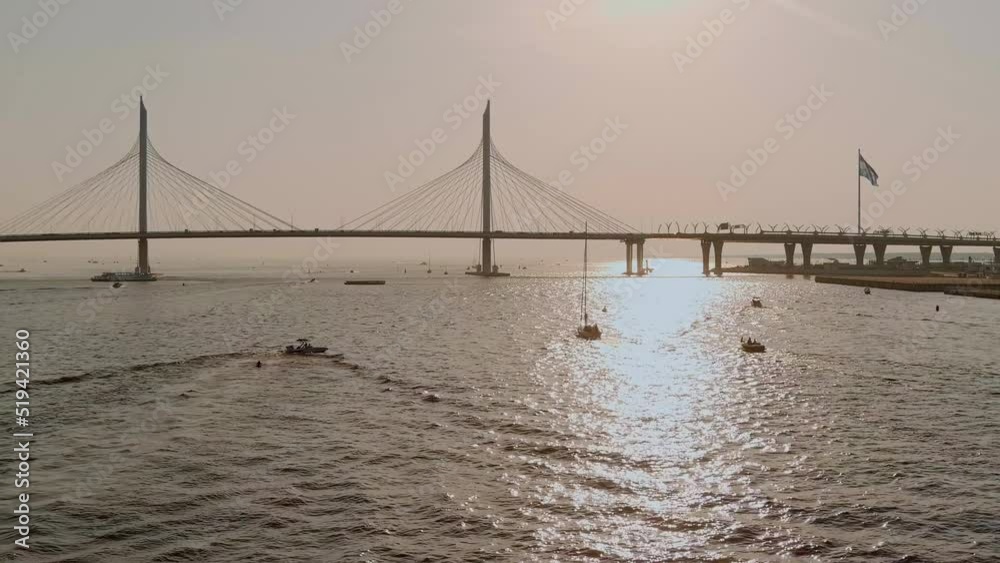 Cable-stayed bridge at sunset, car traffic on the highway over water, magic reflection of sun in water, water navigation, boats and yachts Cable-stayed bridge at sunset, car traffic on the highway over water, magic reflection of sun in water, water navigation, boats and yachts