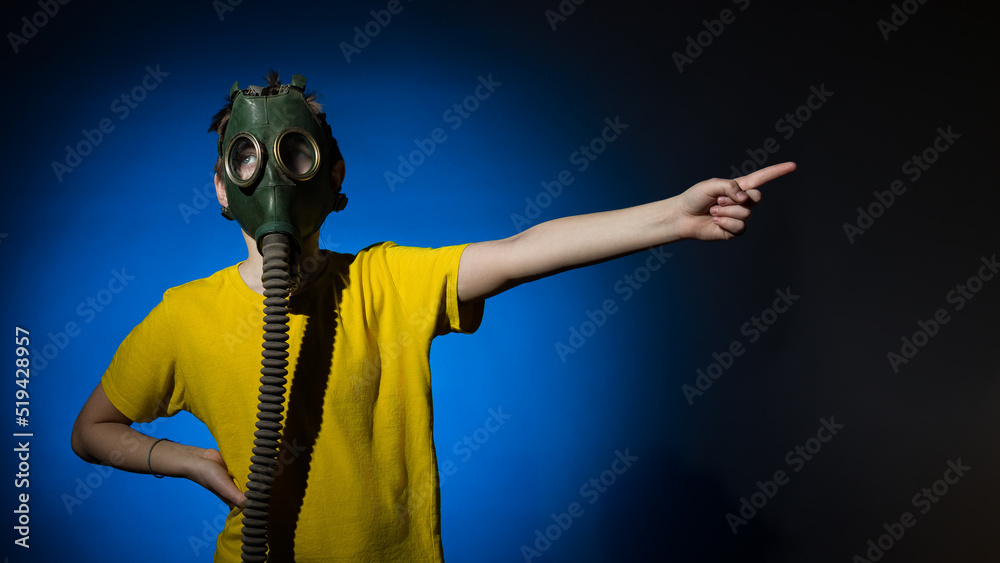 a boy in a gas mask points his finger to the side on a blue background