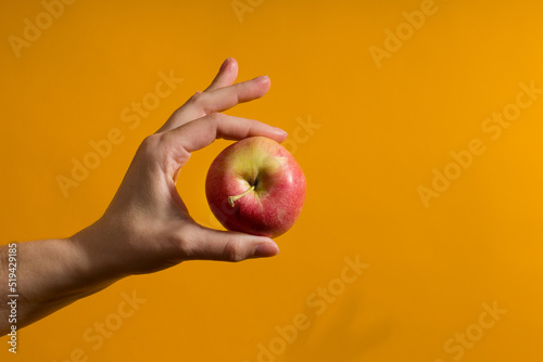 female hand holding red apple on yellow background with copy space