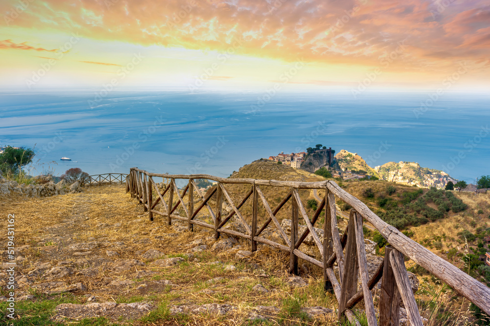 mountain landscape with a hiking trail leading to a mountain town and beautiful blue seashore far away