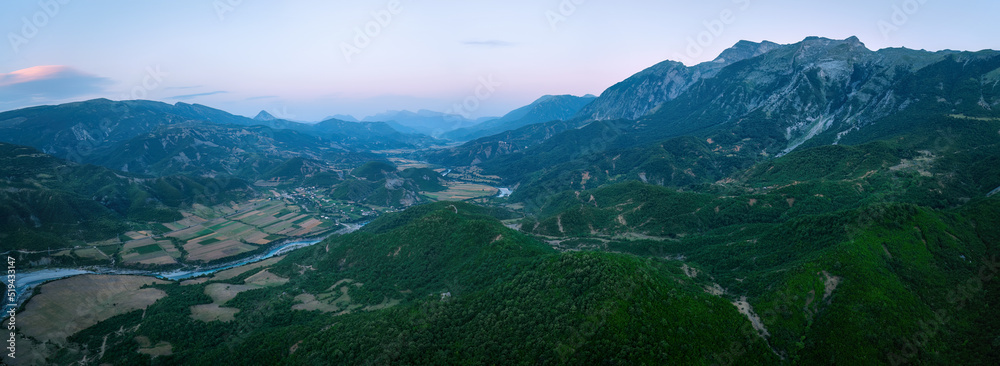 Panoramic landscape, aerial view of the Vjosë river and valley against evening sky. Turquoise water, green valley, sunset sky, steep mounatins, rafting site. Travelling Albania. Panoramic landscape, aerial view of the Vjosë river and valley against evening sky. Turquoise water, green valley, sunset sky, steep mounatins, rafting site. Travelling Albania.
