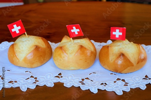 Traditional Swiss buns with a pattern in the shape of the Swiss flag is baked on the eve of the Swiss National Day on August 1st. Buns lie on a wooden table covered with a napkin with the embroidery. photo