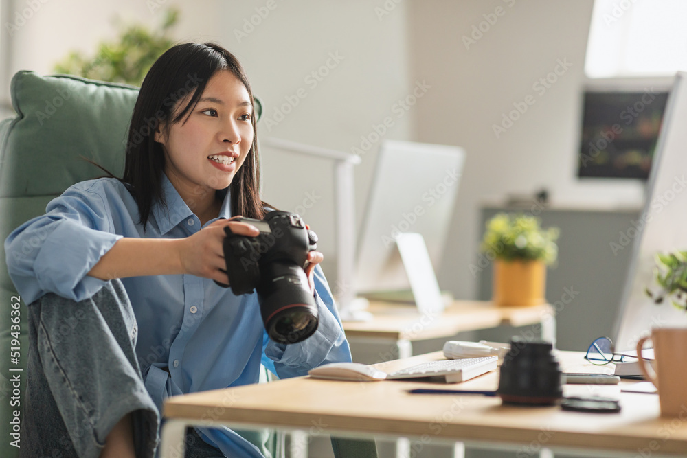Cheerful Vietnamese Woman Photographer Holding Photocamera Sitting At Workplace Cheerful Vietnamese Woman Photographer Holding Photocamera Sitting At Workplace