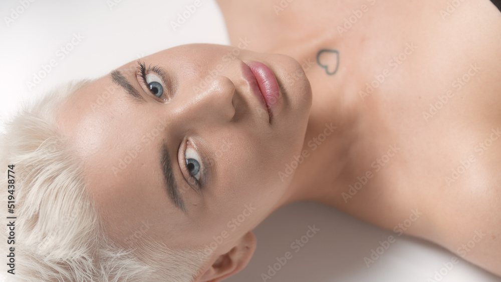 Good-looking young slim Caucasian woman with short light hair looks at the camera on white background | Eye care concept