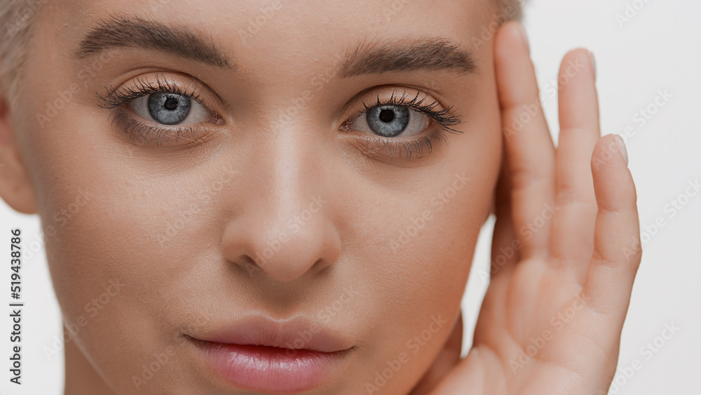 Beautiful young slim blond Caucasian woman touches her face looking at the camera on white background | Face hydration concept Beautiful young slim blond Caucasian woman touches her face looking at the camera on white background | Face hydration concept