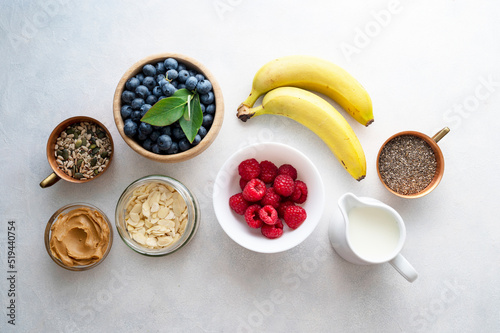 Banana and berry smoothie ingredients made from fresh banana, blueberry, raspberry, milk, peanut butter, chia seeds, almond flakes. Top view