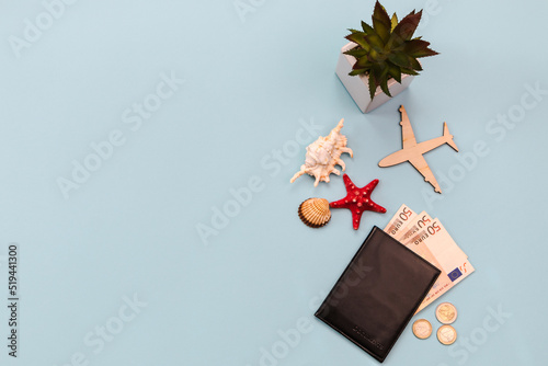 wooden airplane, passport, banknotes and euro coins, shells on a blue background. Travel concept.

