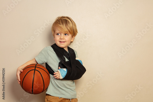 Cute blond boy with broken hand holding basketball ball