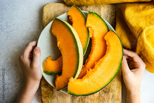 Overhead view of a person holding a plate with slices of cantaloupe melon