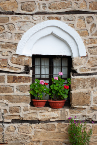 A village in Arbanasi, Bulgaria, has rebuilt an old medieval structure of a church and home. You are viewing the stone walls and window trim holding geranium plants, part of a heritage tour.