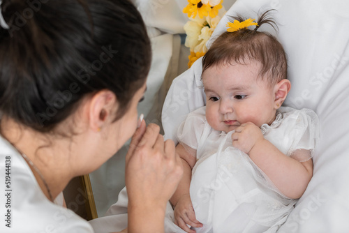 latina mother caressing and pampering her beautiful baby girl. woman pampering a beautiful baby girl lying on her crib, baby looking away from the crib, baby looking distractedly elsewhere. photo