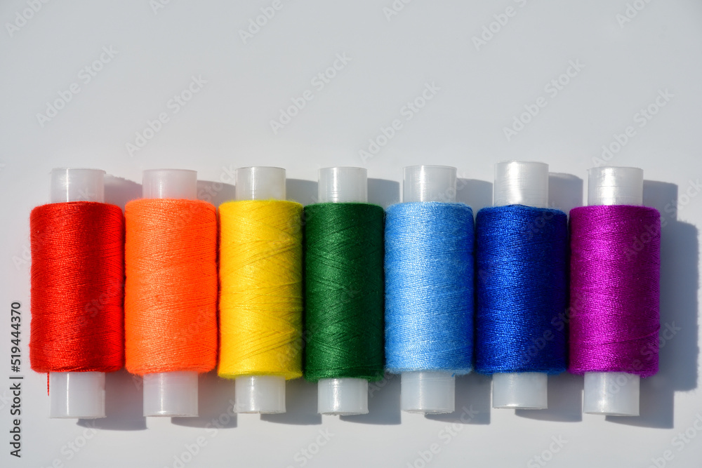 Spools of sewing thread of seven colors of the rainbow close-up on a light background Spools of sewing thread of seven colors of the rainbow close-up on a light background