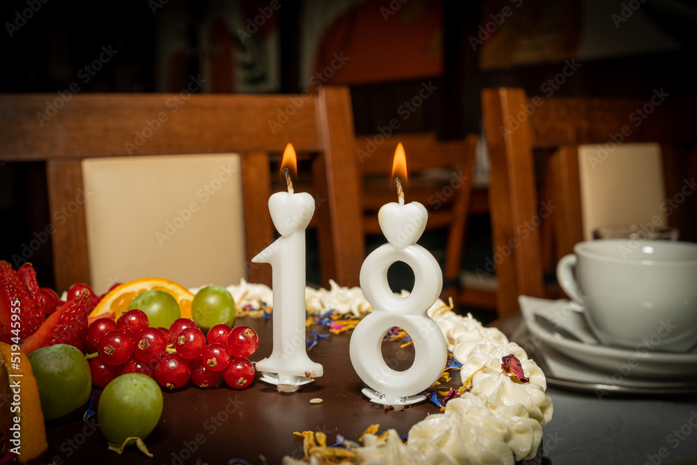 Happy birthday greetings for 18 years old from white numbers against the dark background, copy space. Burning candles for eighteen years on  the chocolate cake