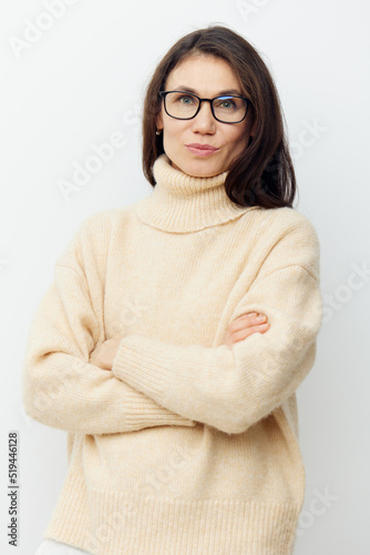 portrait of a beautiful, happy, neat woman in a beige turtleneck sweater and black-rimmed glasses, standing on a light background sideways to the camera and crossing her arms over her chest