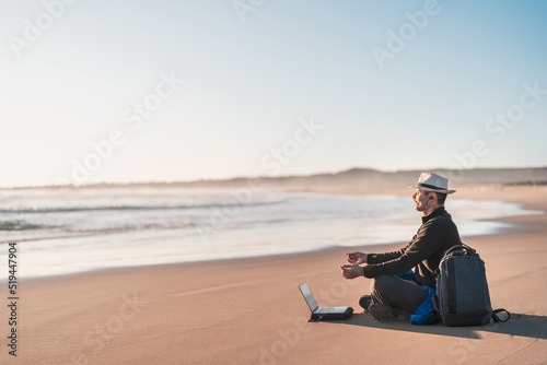 digital nomad sitting on the beach meditating with his laptop on the shore of the beach at sunset