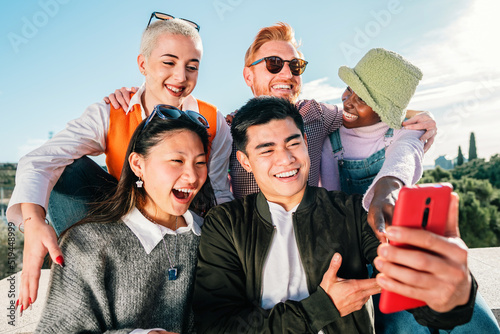 Group of friends watching a video in smartphone smiling and having fun together outdoor. © Jose Calsina