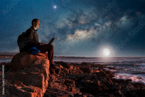 digital nomad sitting on the beach working with his laptop on the rocks of the beach at night