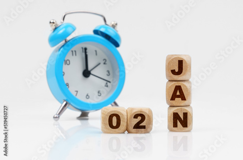 Wooden cube calendar for January 2, next to a blue alarm clock.