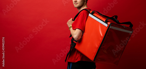 Portrait of young courier. Delivery man in uniform with thermo backpack isolated on red background. Fast home delivery. Online order.