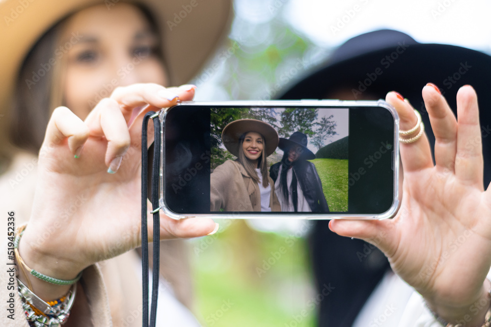 portrait of two smiling young women in hats taking a selfie in the park