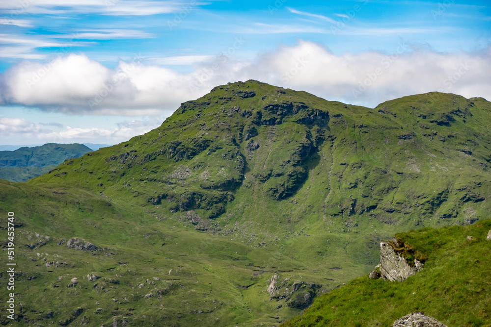 Fototapeta premium View of mountain peaks in the Trossachs National Park from the top of a hill. Beautiful lush green summer mountainous landscape in Scotland