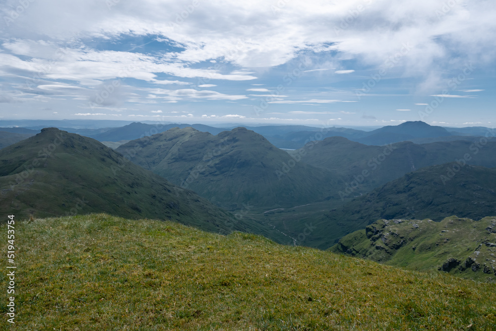 View of mountain peaks in the Trossachs National Park from the top of a hill.  Beautiful lush green summer mountainous landscape in Scotland