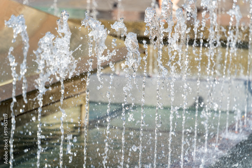 Selective focus, water jets of the city fountain on a sunny day on a blurred background, hot summer weather in the city