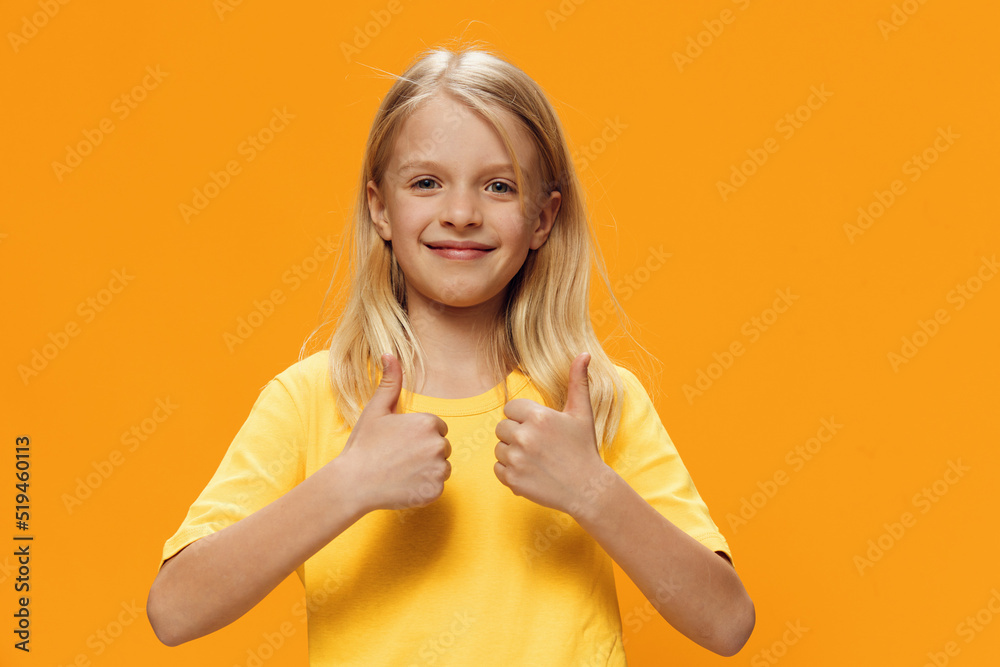 a cute, happy girl in yellow clothes stands on a yellow background and smiles cutely at the camera showing thumbs up. Horizontal studio photography on a plain background with empty space a cute, happy girl in yellow clothes stands on a yellow background and smiles cutely at the camera showing thumbs up. Horizontal studio photography on a plain background with empty space