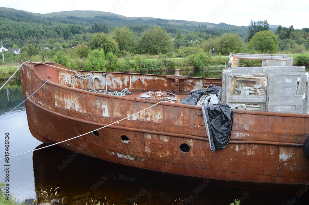 A boat that has seen better days on the Caledonian canal, Fort Augustus,, the rusting decay contrasting with the vibrancy of the surounding countryside