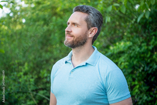 Portrait of handsome guy in blue tshirt looking aside natural background