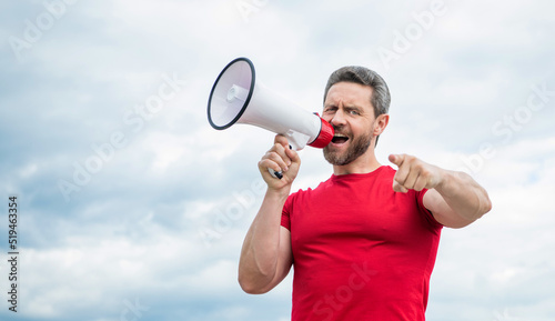 man in red shirt shout in loudspeaker on sky background. point finger photo