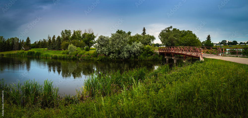 Wascana Creek pond and bridge adjacent to the tranquil hilly meadow with footpaths at A.E. Wilson Park in Regina, Saskatchewan, Canada. A rainy day landscape at the city park.