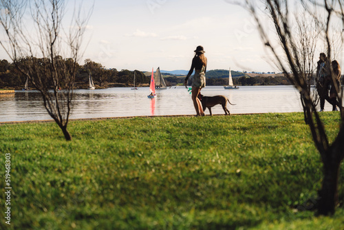 woman walking dog near lake with sailing