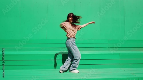 Young woman dancing hip hop on green background wall. Modern dance choreography. Female professional dancer showing dance movings. Musical video. photo