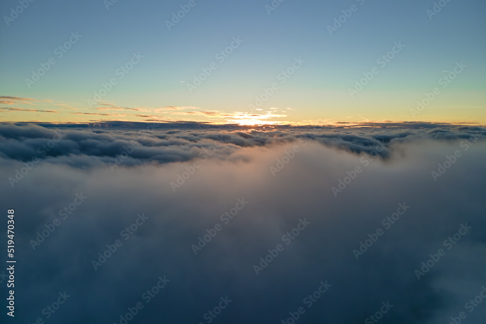 Aerial view from above at high altitude of dense puffy cumulus clouds flying in evening. Amazing sunset from airplane window point of view