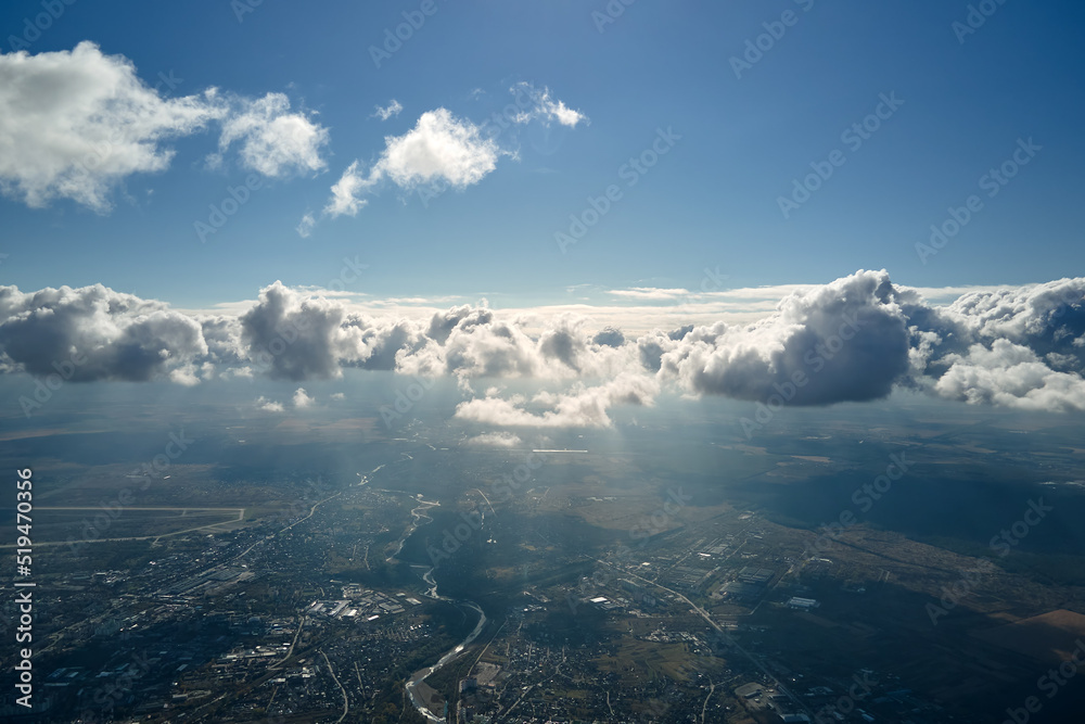 Aerial view from airplane window at high altitude of distant city covered with white puffy cumulus clouds