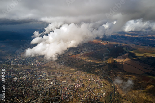 Aerial view from airplane window at high altitude of distant city covered with white puffy cumulus clouds © bilanol