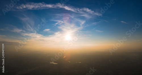 Aerial view from airplane window at high altitude of earth covered with white thin layer of misty haze and distant clouds at sunset