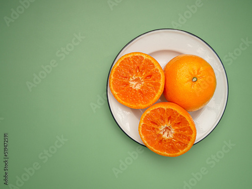 Top view of oranges cut half and whole on a white dish over a green background
