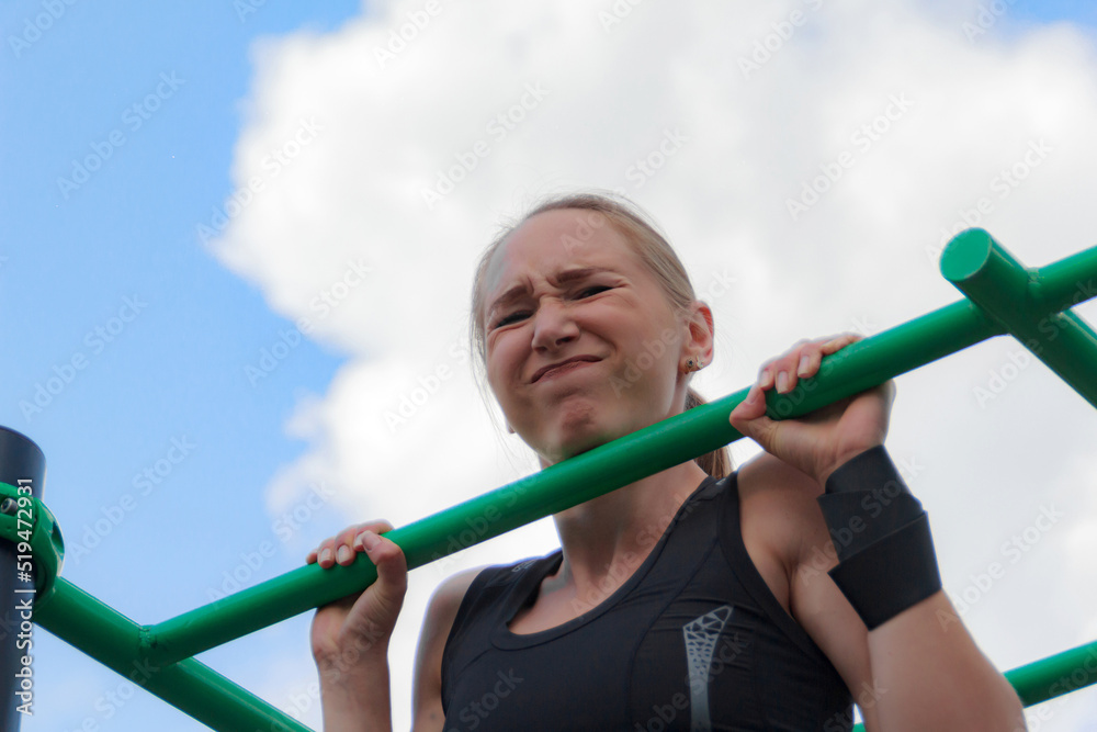Young blonde woman in a dark tracksuit is engaged in fitness on the sports ground